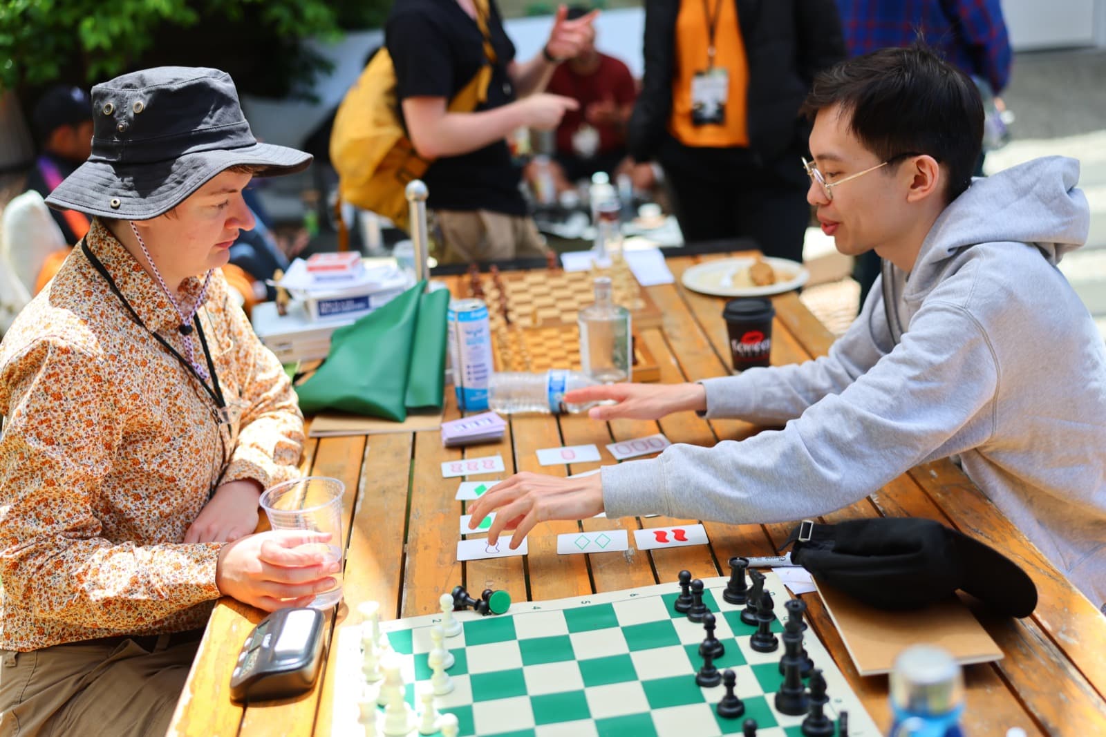 Two players at an outdoor wooden table with chess and Bananagrams.