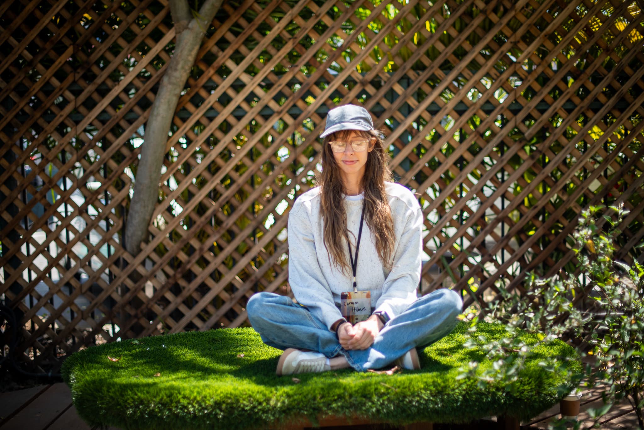 A person sits quietly behind a shaded wooden counter with drinks and plants nearby.
