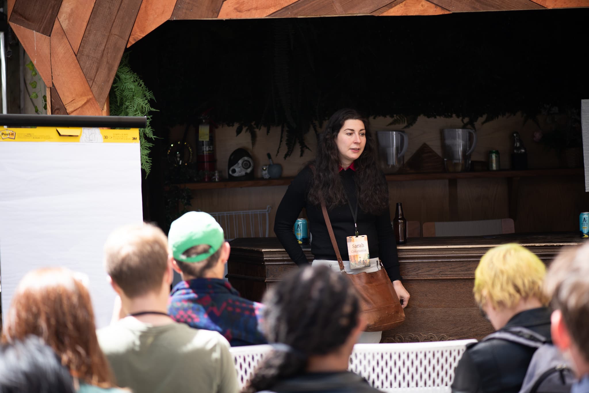 A speaker sits cross-legged in a courtyard gesturing toward a whiteboard listing science-fiction sources.